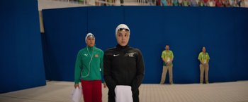 Movie still from “The Swimmers” (2022), directed by Sally El Hosaini – A young man wearing a swimming cap and a towel; Medium shot, Over the shoulder angle