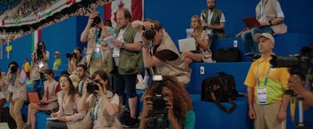 Movie still from “The Swimmers” (2022), directed by Sally El Hosaini – A group of people taking pictures in a stadium; Wide shot, Low angle