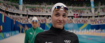 Movie still from “The Swimmers” (2022), directed by Sally El Hosaini – A woman in a swimming cap and goggles; Close Up shot, Over the shoulder angle