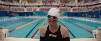 Movie still from “The Swimmers” (2022), directed by Sally El Hosaini – A woman in a swimming cap and goggles in front of a swimming pool; Close Up shot, High angle