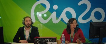 Movie still from “The Swimmers” (2022), directed by Sally El Hosaini – Two people sitting at a table in front of a rio sign; Medium shot, Over the shoulder angle