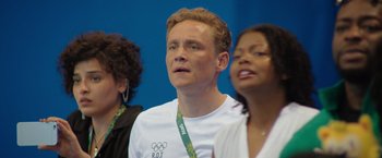 Movie still from “The Swimmers” (2022), directed by Sally El Hosaini – A man in a white t - shirt is standing next to two other women; Close Up shot, Over the shoulder angle