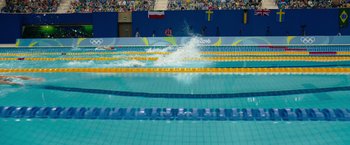 Movie still from “The Swimmers” (2022), directed by Sally El Hosaini – A swimming pool that has a lot of people in it; Extreme Wide shot, Overhead angle