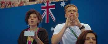 Movie still from “The Swimmers” (2022), directed by Sally El Hosaini – A man and a woman watching something while holding their hands to their face; Medium shot, Over the shoulder angle