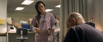 Movie still from “Elysium” (2013), directed by Neill Blomkamp – A woman in a purple lab coat holding a clipboard; Medium shot, Over the shoulder angle