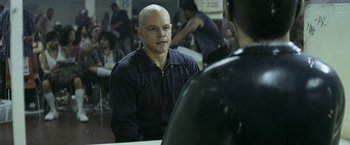 Movie still from “Elysium” (2013), directed by Neill Blomkamp – A man sitting in front of another man in front of a crowd; Close Up shot, Over the shoulder angle