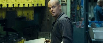 Movie still from “Elysium” (2013), directed by Neill Blomkamp – A man with a bald head standing next to a table; Close Up shot, Low angle
