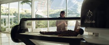 Movie still from “Elysium” (2013), directed by Neill Blomkamp – A woman standing next to a man laying on a bed; Wide shot, High angle