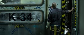 Movie still from “Elysium” (2013), directed by Neill Blomkamp – A man in a black jacket is standing in front of a train; Close Up shot, Over the shoulder angle