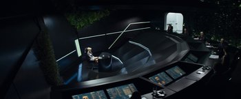 Movie still from “Elysium” (2013), directed by Neill Blomkamp – A woman sitting on a chair in a room with many screens; Wide shot, High angle