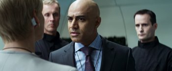 Movie still from “Elysium” (2013), directed by Neill Blomkamp – A man in a suit and tie looking at the camera; Close Up shot, Over the shoulder angle