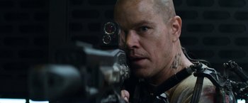 Movie still from “Elysium” (2013), directed by Neill Blomkamp – A man with a gun looking into a camera; Close Up shot, Low angle