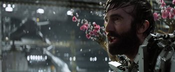 Movie still from “Elysium” (2013), directed by Neill Blomkamp – A man with a beard and flowers in the background; Close Up shot, Over the shoulder angle