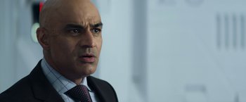 Movie still from “Elysium” (2013), directed by Neill Blomkamp – A man in a suit and tie looking at the camera; Close Up shot, Over the shoulder angle