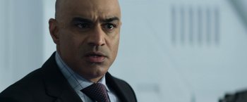 Movie still from “Elysium” (2013), directed by Neill Blomkamp – A person wearing a suit and tie; Close Up shot, Over the shoulder angle