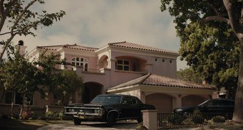 Movie still from “The Tax Collector” (2020), directed by David Ayer – A car is parked in front of a pink house; Extreme Wide shot, High angle