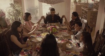 Movie still from “The Tax Collector” (2020), directed by David Ayer – A group of people sitting around a dinner table holding hands; Wide shot, High angle