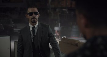 Movie still from “The Tax Collector” (2020), directed by David Ayer – A man in a suit and tie standing in a room; Medium shot, Over the shoulder angle