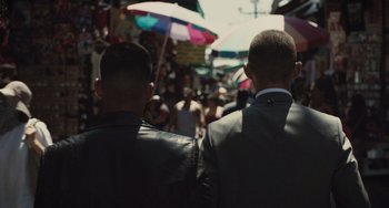 Movie still from “The Tax Collector” (2020), directed by David Ayer – Two men are standing in a crowd of people holding umbrellas; Close Up shot, Over the shoulder angle