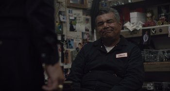 Movie still from “The Tax Collector” (2020), directed by David Ayer – An older man sitting in front of a wall of pictures; Medium shot, Over the shoulder angle