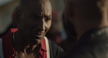 Movie still from “The Tax Collector” (2020), directed by David Ayer – An older man wearing a red shirt is looking at the camera; Close Up shot, Over the shoulder angle