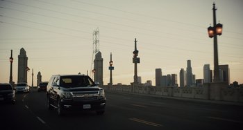 Movie still from “The Tax Collector” (2020), directed by David Ayer – A truck driving down a road near a bridge; Wide shot, Low angle