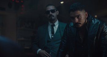 Movie still from “The Tax Collector” (2020), directed by David Ayer – A man in a suit standing next to another man in a leather jacket; Medium shot, Low angle
