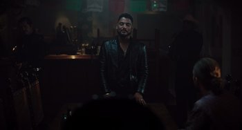 Movie still from “The Tax Collector” (2020), directed by David Ayer – A man in a leather jacket standing at a table; Medium shot, Over the shoulder angle