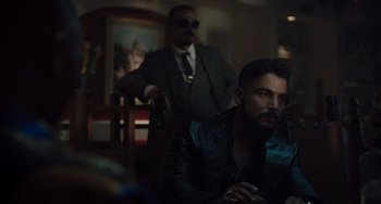 Movie still from “The Tax Collector” (2020), directed by David Ayer – A man sitting in front of another man in a suit; Medium shot, Over the shoulder angle