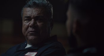 Movie still from “The Tax Collector” (2020), directed by David Ayer – An older man wearing a name tag in front of another man; Close Up shot, Over the shoulder angle