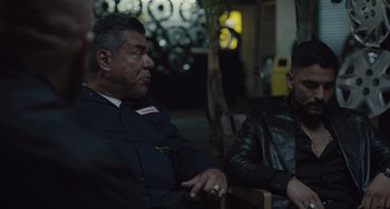 Movie still from “The Tax Collector” (2020), directed by David Ayer – A man sitting next to another man wearing a leather jacket; Medium shot, Over the shoulder angle