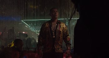 Movie still from “The Tax Collector” (2020), directed by David Ayer – A man wearing a colorful shirt standing next to a wall; Medium shot, Low angle