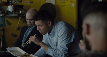 Movie still from “The Tax Collector” (2020), directed by David Ayer – A man sitting at a table with a plate of food in front of him; Medium shot, Over the shoulder angle