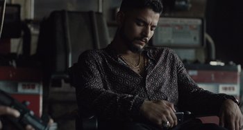 Movie still from “The Tax Collector” (2020), directed by David Ayer – A man sitting in a chair looking at his cell phone; Medium shot, High angle