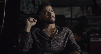 Movie still from “The Tax Collector” (2020), directed by David Ayer – A man with a goatee and a beard is wearing a shirt and a necklace; Close Up shot, Over the shoulder angle