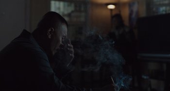 Movie still from “The Tax Collector” (2020), directed by David Ayer – A man smoking a cigarette while sitting in a room; Close Up shot, Over the shoulder angle