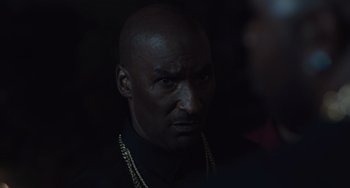 Movie still from “The Tax Collector” (2020), directed by David Ayer – A man in a black shirt and gold chains; Close Up shot, Over the shoulder angle
