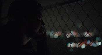 Movie still from “The Tax Collector” (2020), directed by David Ayer – A man looking out a chain link fence at night; Close Up shot, Low angle