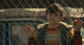 Movie still from “The Tender Bar” (2021), directed by George Clooney – A young boy standing in front of a chain link fence; Close Up shot, Over the shoulder angle