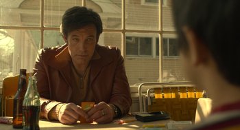 Movie still from “The Tender Bar” (2021), directed by George Clooney – A man sitting at a table holding a box; Medium shot, Low angle