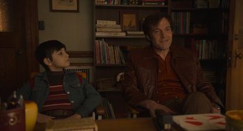 Movie still from “The Tender Bar” (2021), directed by George Clooney – A man and a boy sitting at a table in front of a book shelf; Medium shot, Over the shoulder angle