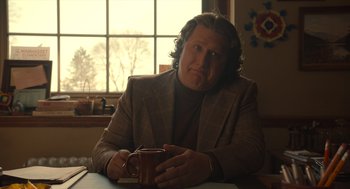Movie still from “The Tender Bar” (2021), directed by George Clooney – A man sitting at a table holding a coffee mug; Medium shot, Low angle
