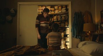 Movie still from “The Tender Bar” (2021), directed by George Clooney – A man and a boy in front of a bookcase; Medium shot, High angle