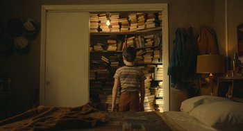 Movie still from “The Tender Bar” (2021), directed by George Clooney – A boy standing in front of a book closet; Medium shot, Overhead angle