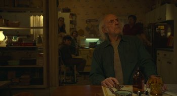 Movie still from “The Tender Bar” (2021), directed by George Clooney – An older man sitting at a table in front of people; Medium shot, Low angle
