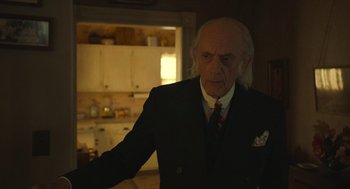 Movie still from “The Tender Bar” (2021), directed by George Clooney – An older man in a suit and tie in a kitchen; Medium shot, Over the shoulder angle