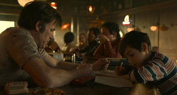 Movie still from “The Tender Bar” (2021), directed by George Clooney – A group of people sitting at a table writing on paper; Medium shot, Over the shoulder angle