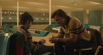 Movie still from “The Tender Bar” (2021), directed by George Clooney – A man and a boy sitting in a bowling alley; Medium shot, Over the shoulder angle