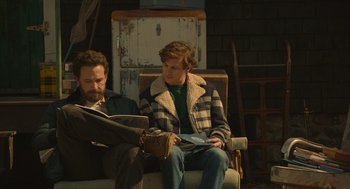 Movie still from “The Tender Bar” (2021), directed by George Clooney – Two people sitting in a chair reading a magazine; Medium shot, Over the shoulder angle