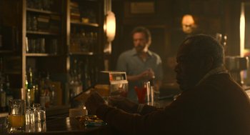 Movie still from “The Tender Bar” (2021), directed by George Clooney – A man sitting at a bar with a glass of wine; Medium shot, Over the shoulder angle